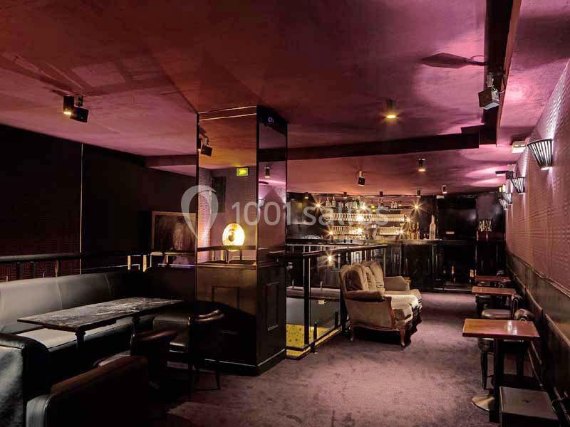 Intérieur d'un bar lounge avec éclairage tamisé, mobilier sombre, tables basses et un comptoir en arrière-plan.
