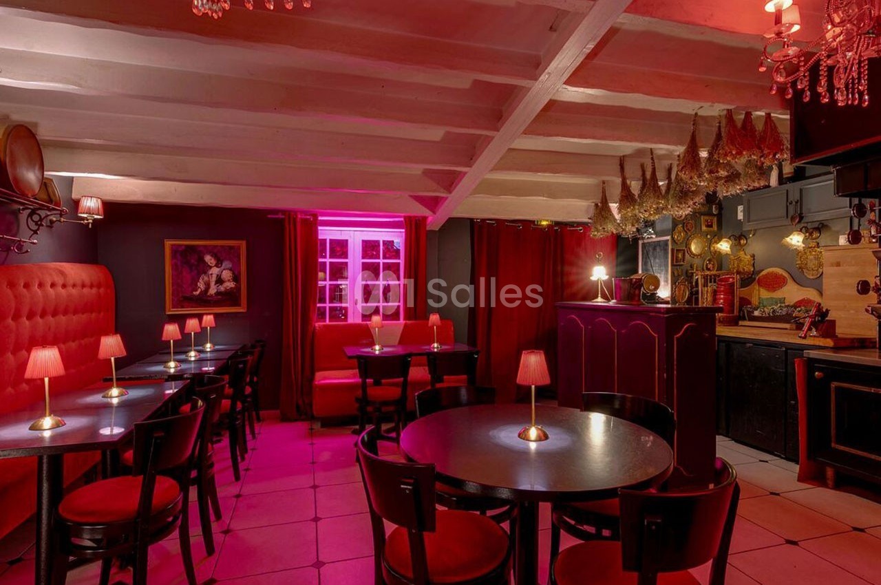 Salle de restaurant à l'éclairage tamisé rose, avec tables rondes, chaises noires et décorations murales.