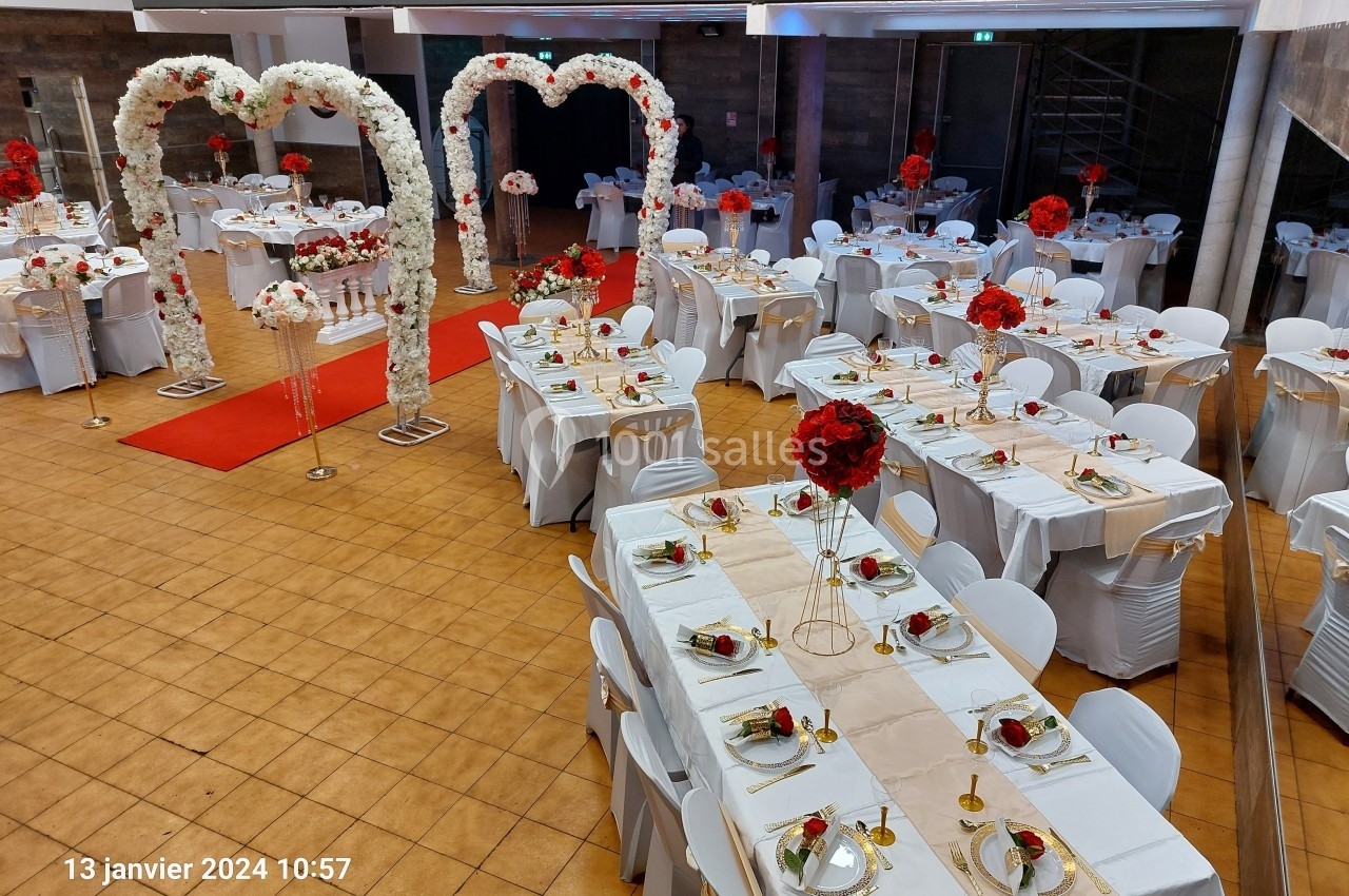 Salle de réception décorée avec des tables dressées, des arches fleuries blanches et des centres de table rouges.