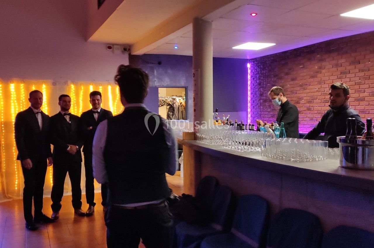 Un groupe d'hommes en costume pose près d'un bar éclairé, avec un barman préparant des boissons.