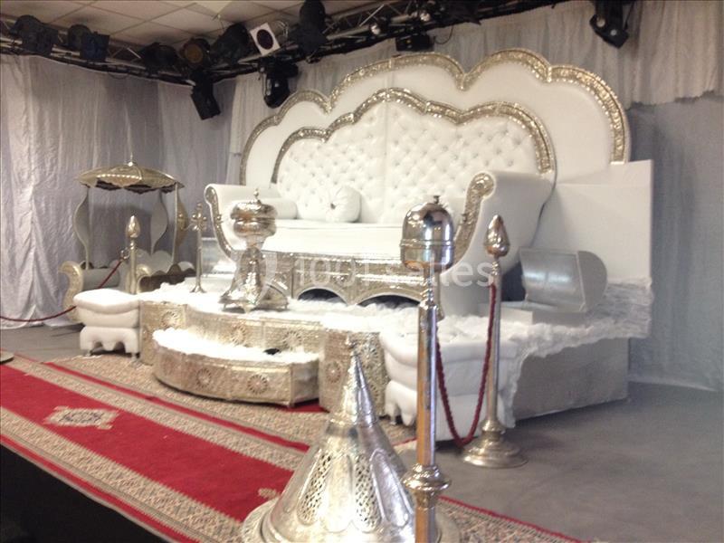 Décor de cérémonie avec un trône blanc capitonné, des ornements argentés et un tapis rouge sur une scène.
