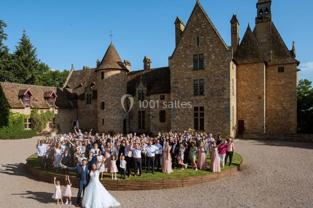 Un grand groupe de personnes posant devant un château en pierre sous un ciel bleu.