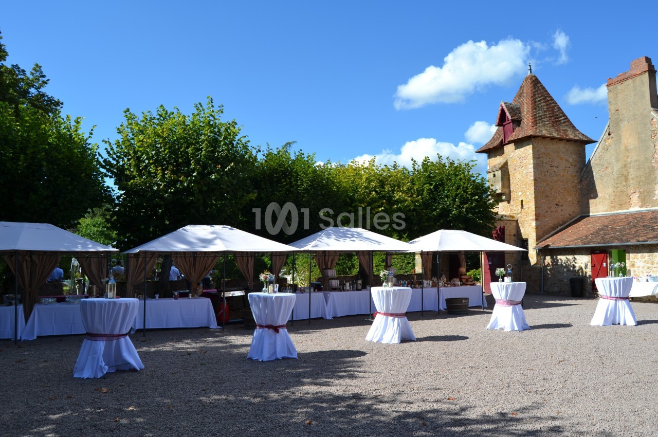 Tentes blanches et tables dressées dans une cour pavée, près d'un bâtiment en pierre avec une tour.