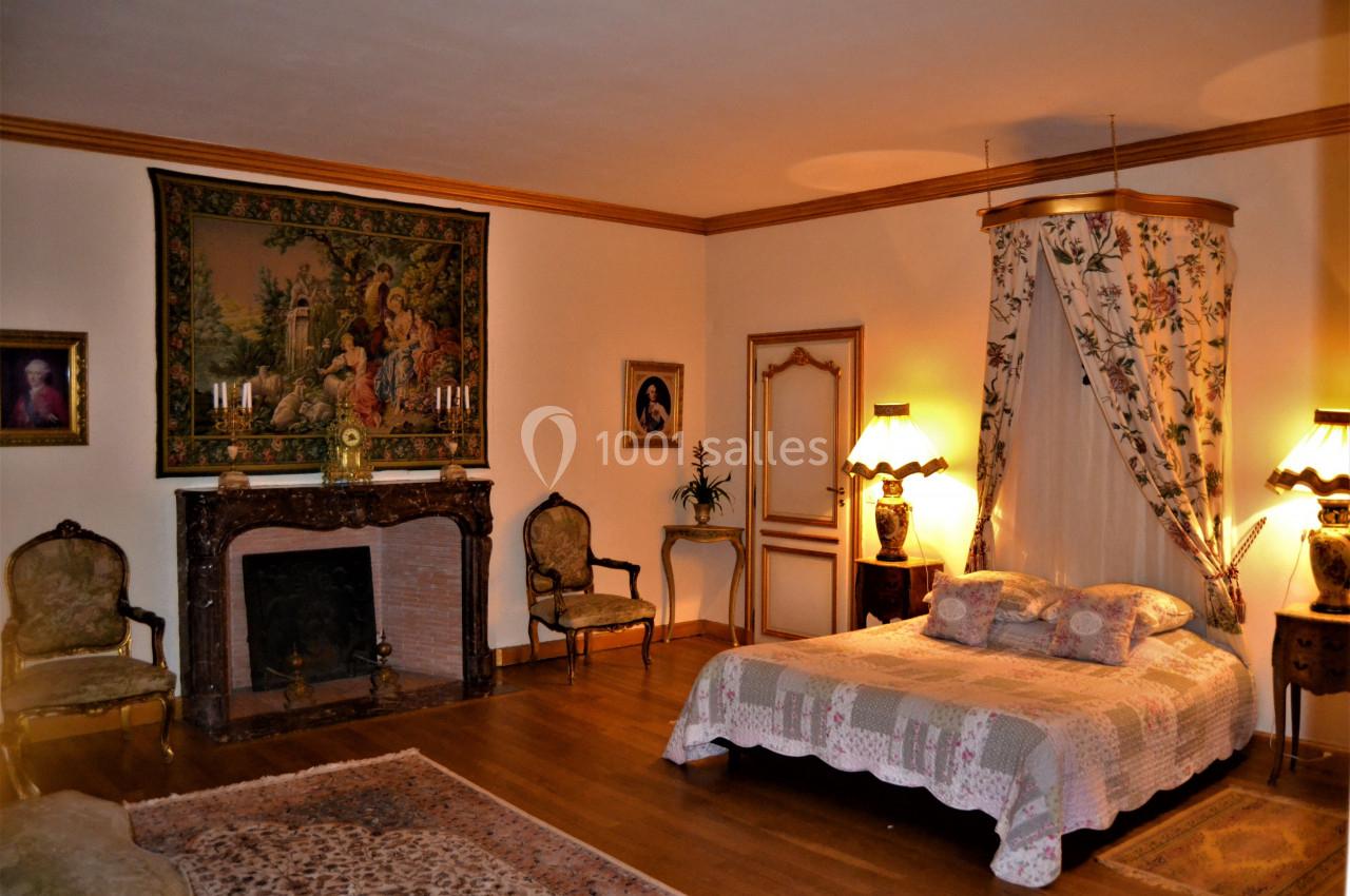 Chambre élégante avec lit à baldaquin, cheminée ornée, tapis au sol et mobilier ancien dans une ambiance chaleureuse.