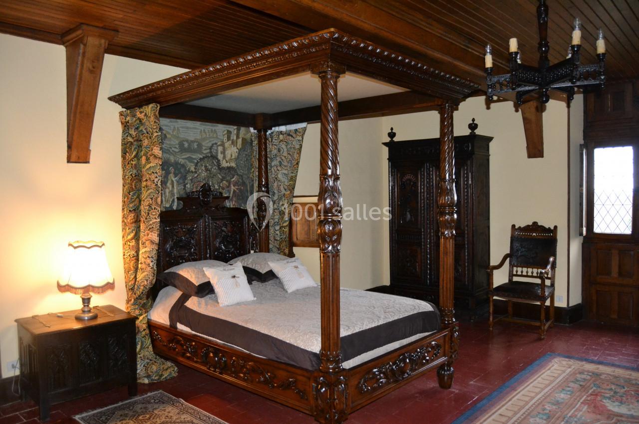 Lit à baldaquin en bois sculpté dans une chambre rustique avec meubles anciens et tapis au sol.