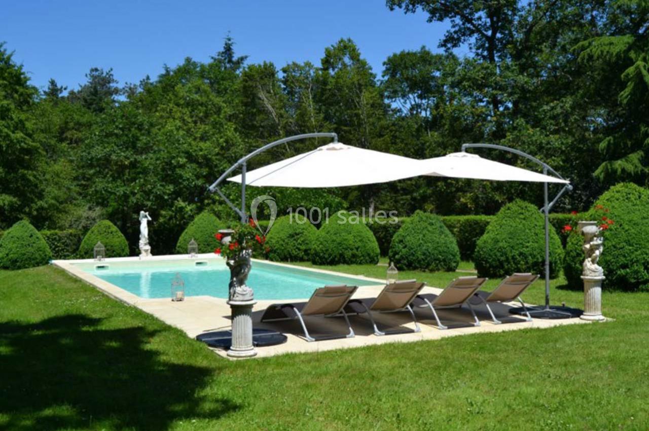 Piscine extérieure entourée de verdure, avec transats alignés et parasols blancs sur une pelouse bien entretenue.