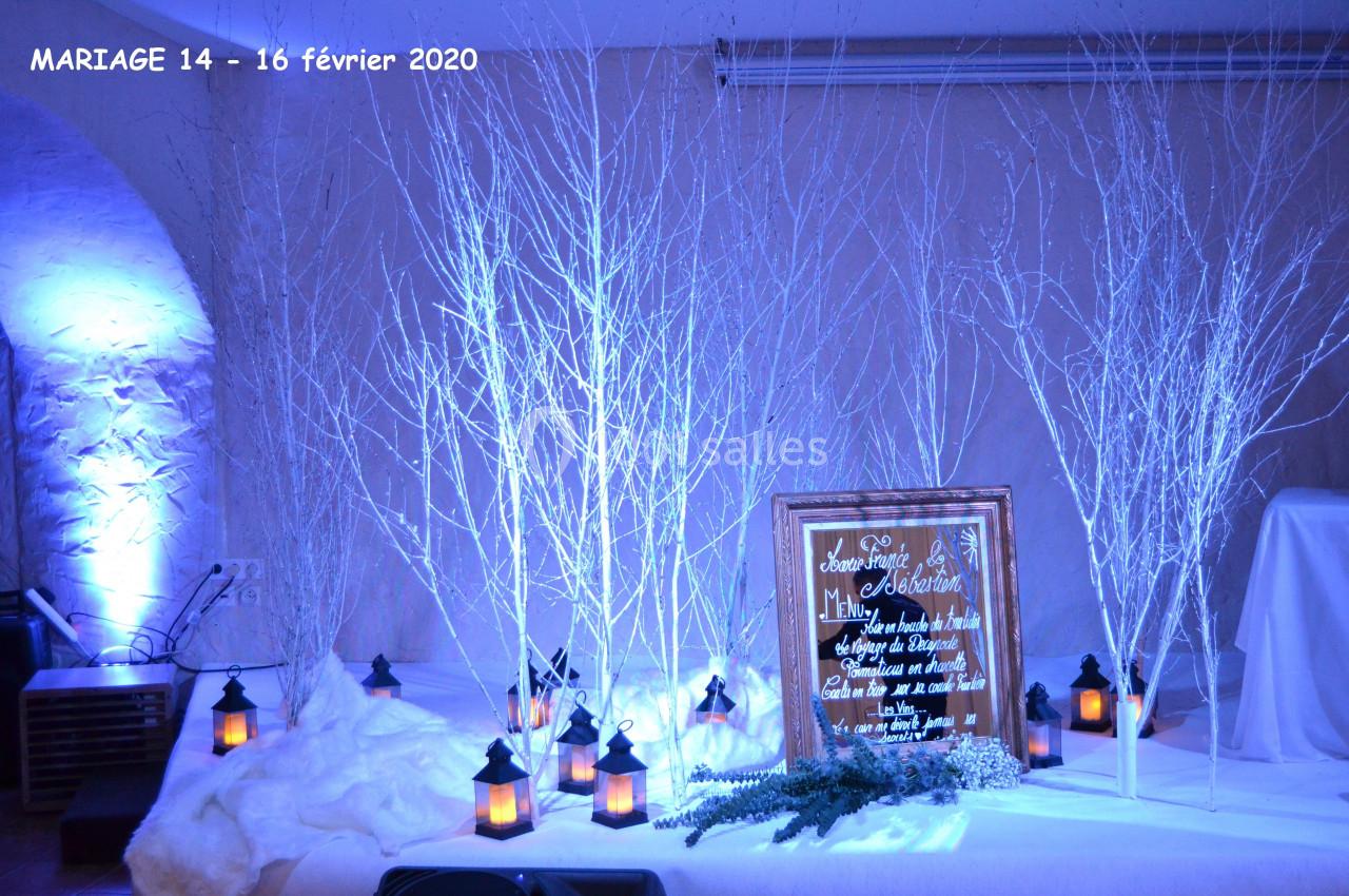 Décoration de mariage hivernale avec branches blanches, lanternes allumées et panneau en bois dans une ambiance bleutée.