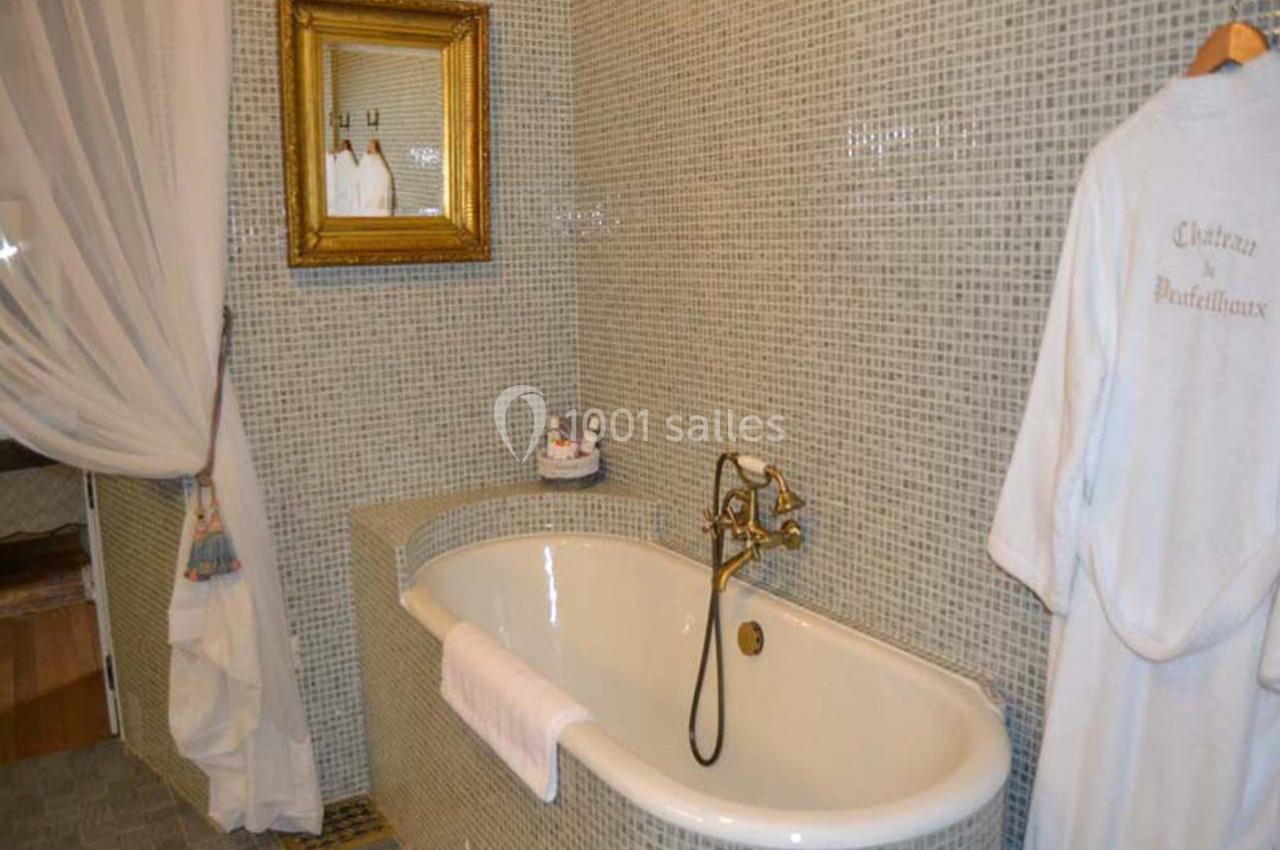 Salle de bain avec baignoire blanche, robinetterie dorée, miroir encadré et murs en mosaïque grise.