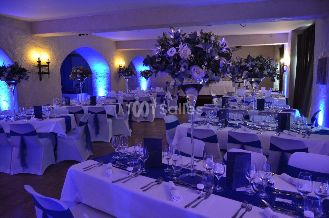 Salle de réception élégamment décorée avec des tables dressées, des fleurs et un éclairage bleu tamisé.