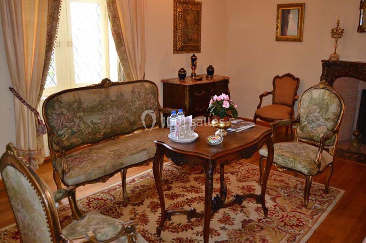 Salon ancien avec mobilier d'époque, comprenant un canapé, des fauteuils, une table en bois et un tapis orné.