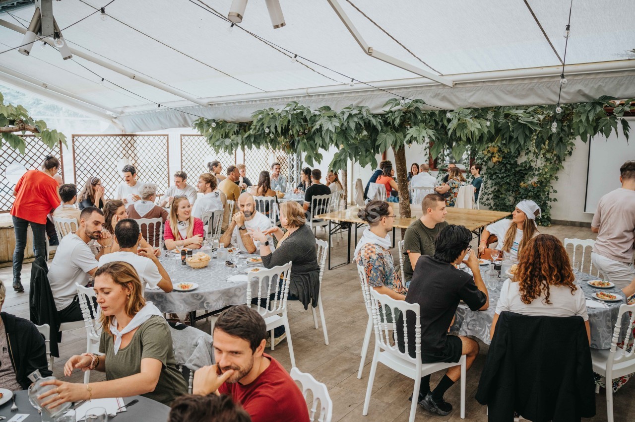 Des personnes assises à des tables dans une grande salle lumineuse, partageant un repas dans une ambiance conviviale.
