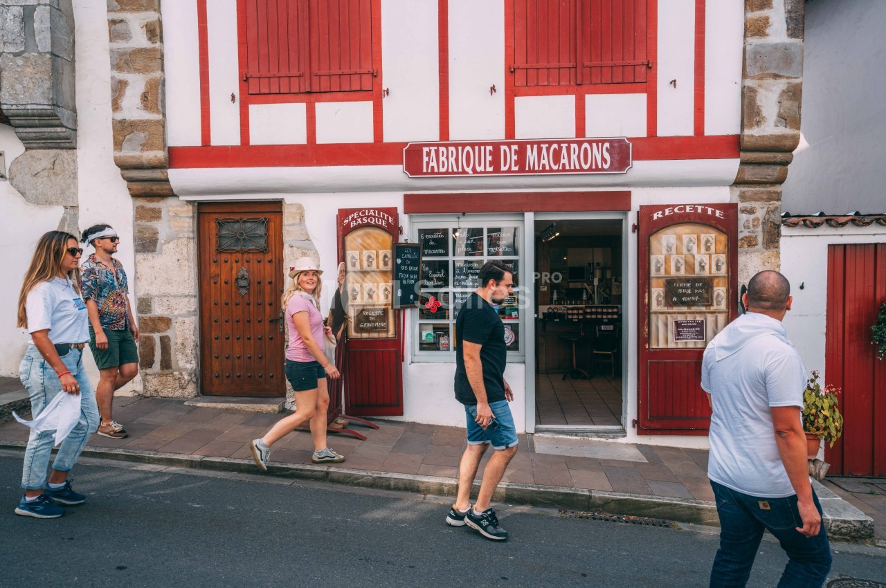 Devanture d'une boutique traditionnelle de macarons avec des passants marchant sur le trottoir.