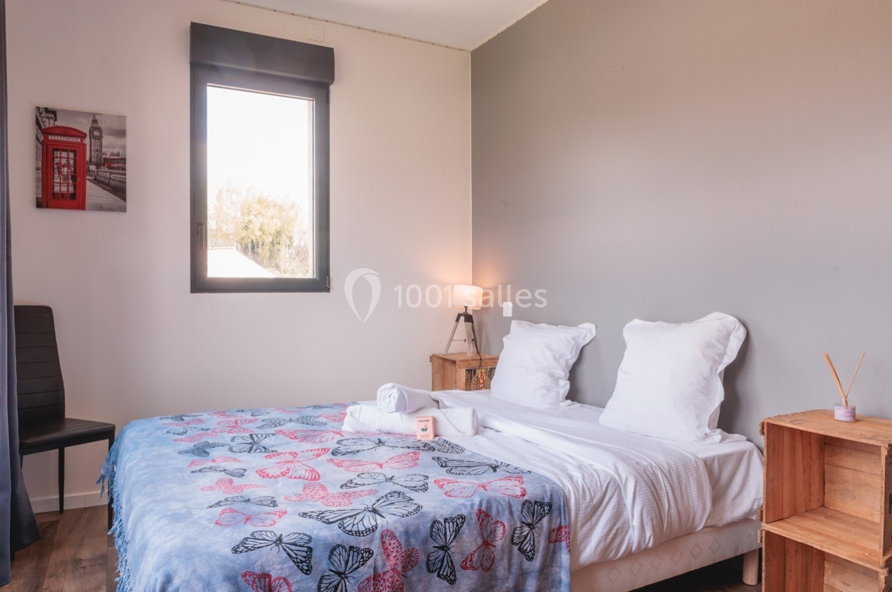 Chambre lumineuse avec lit double, linge plié, table de chevet, lampe allumée et fenêtre donnant sur l'extérieur.