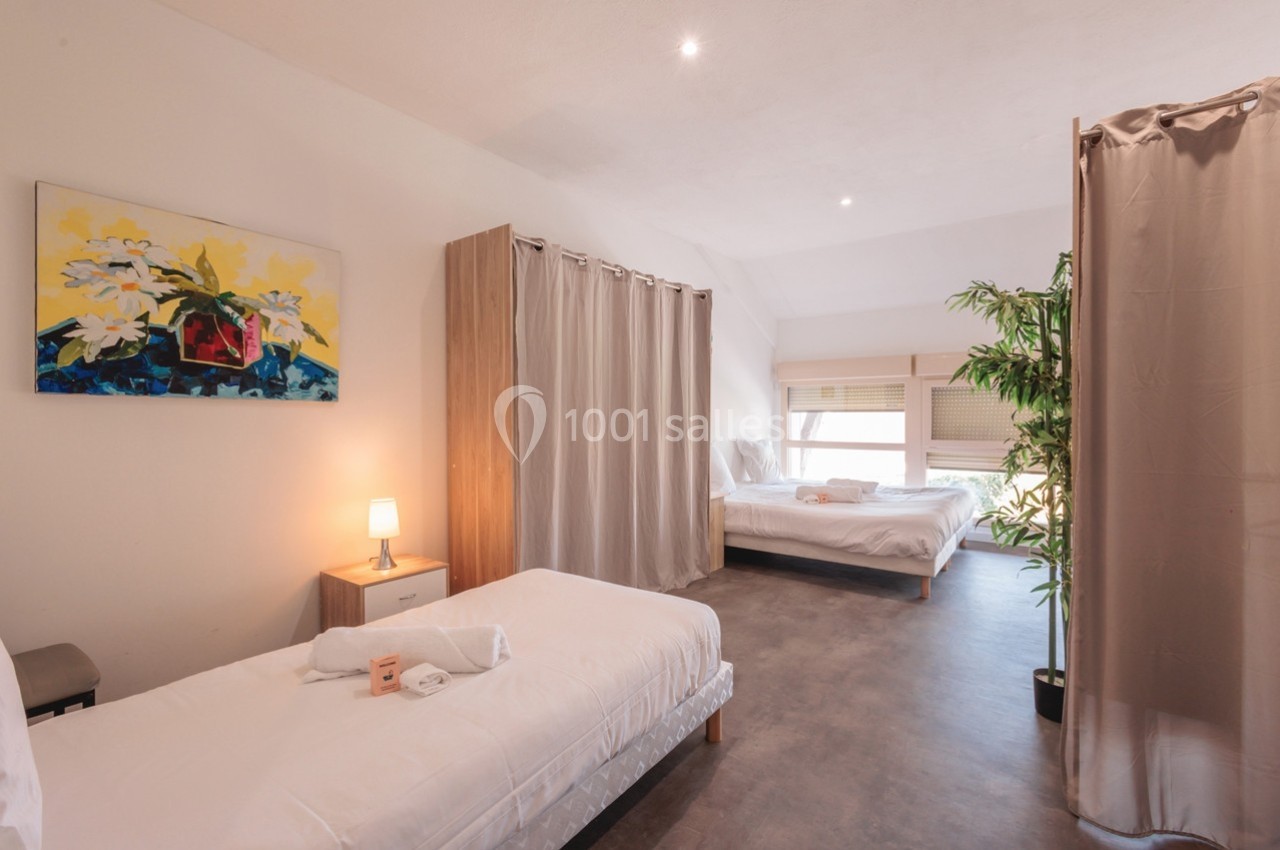 Chambre lumineuse avec deux lits simples, un lit double, des rideaux séparateurs et une décoration minimaliste.