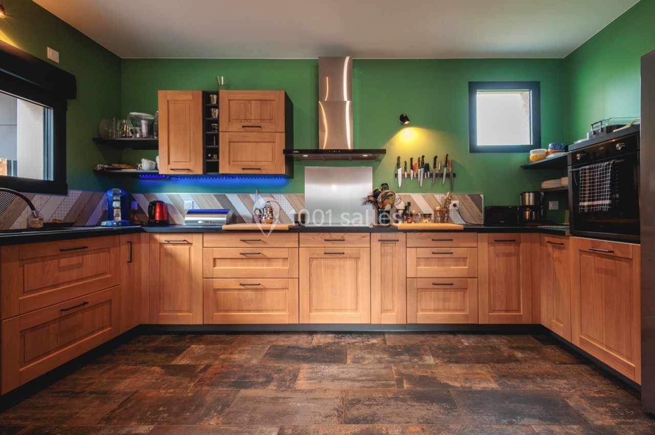 Cuisine moderne avec meubles en bois clair, murs verts, sol foncé et électroménagers intégrés.