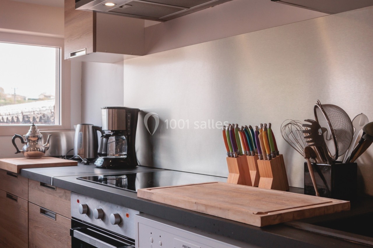 Cuisine moderne avec plan de travail en bois, cafetière, couteaux colorés et ustensiles près d'une fenêtre.