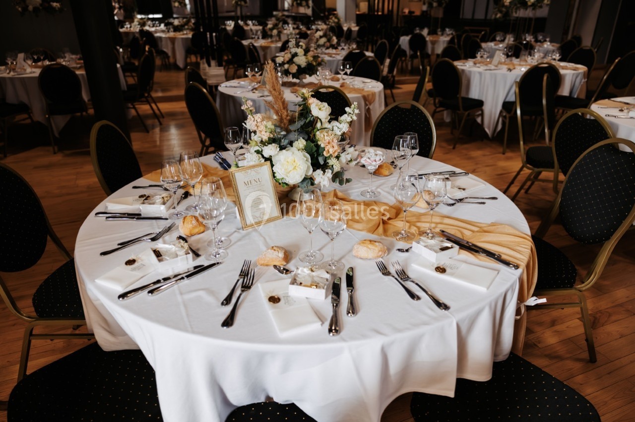 Table élégamment dressée avec nappes blanches, couverts, fleurs et menu, dans une salle de réception.