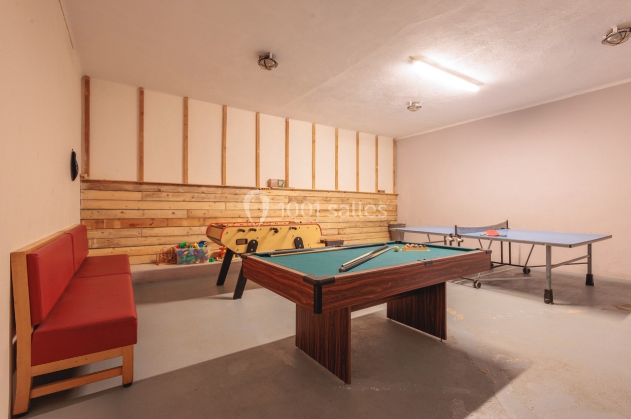 Salle de jeux avec une table de billard, un baby-foot, une table de ping-pong et un banc rouge contre le mur.