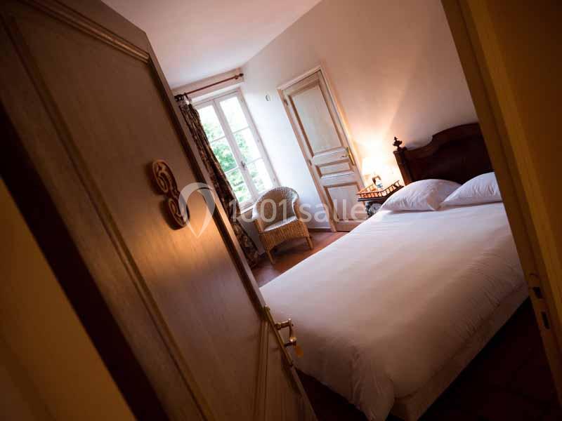 Chambre avec lit double, fauteuil en osier, lampe allumée et fenêtre donnant sur un extérieur verdoyant.