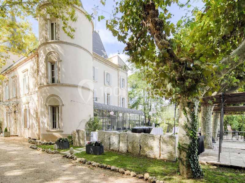 Façade d'un bâtiment ancien entouré d'arbres, avec une terrasse aménagée et des tables dressées à l'extérieur.