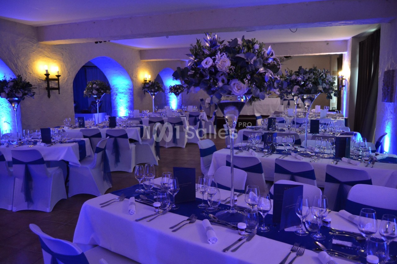 Salle de réception décorée avec des tables dressées, des nappes blanches et des arrangements floraux violets sous un…