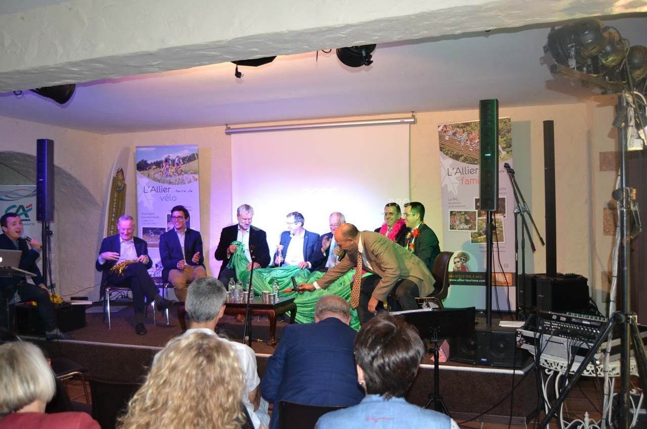 Un groupe de personnes assises sur une scène lors d'une conférence, avec des affiches promotionnelles en arrière-plan.
