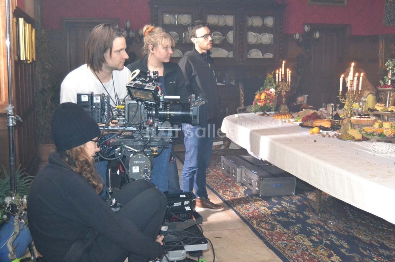 Une équipe de tournage filme une table dressée avec des plats et des chandeliers dans une pièce décorée.