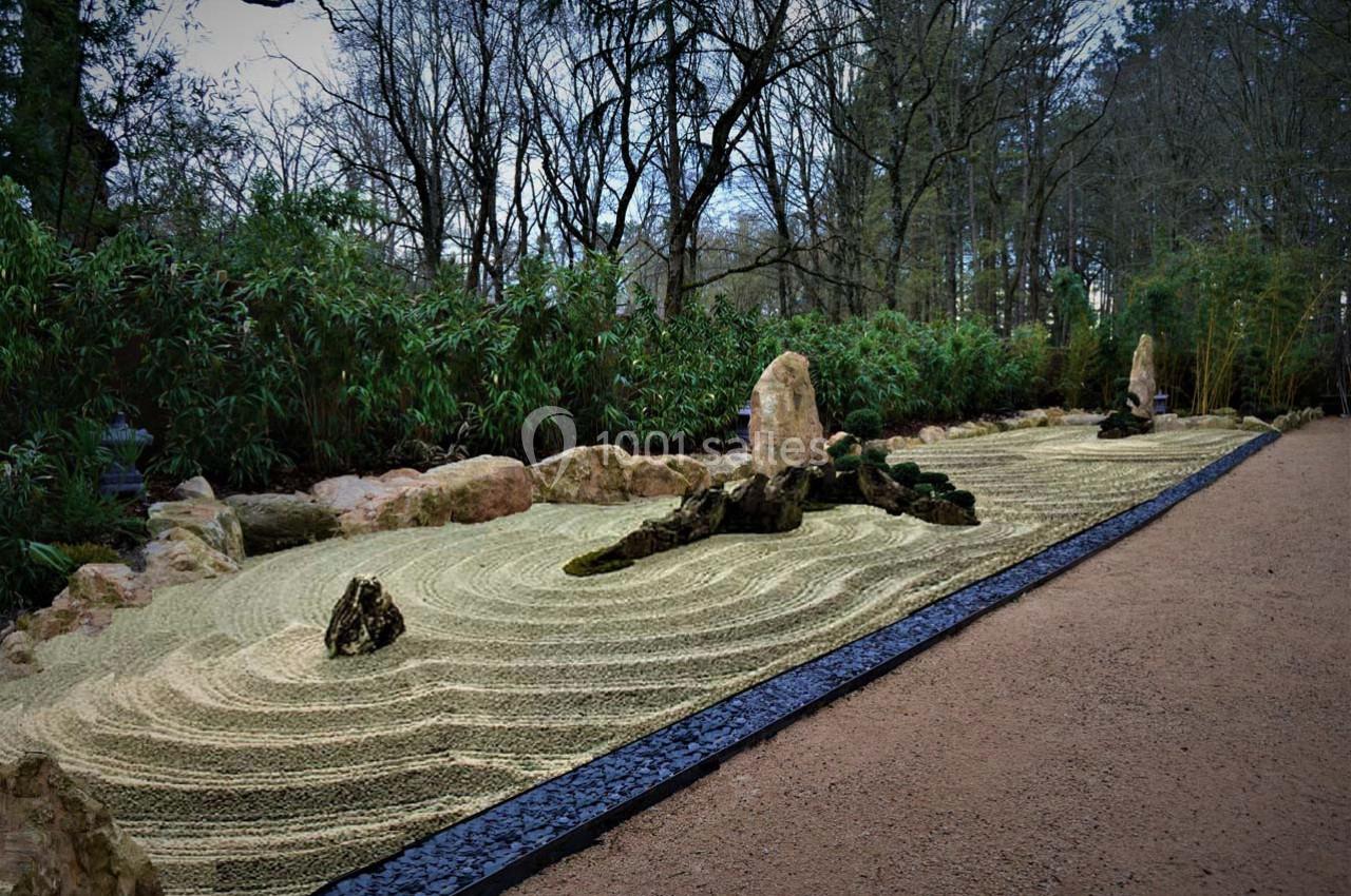 Jardin zen avec gravier ratissé en motifs ondulés, pierres disposées harmonieusement et végétation en arrière-plan.