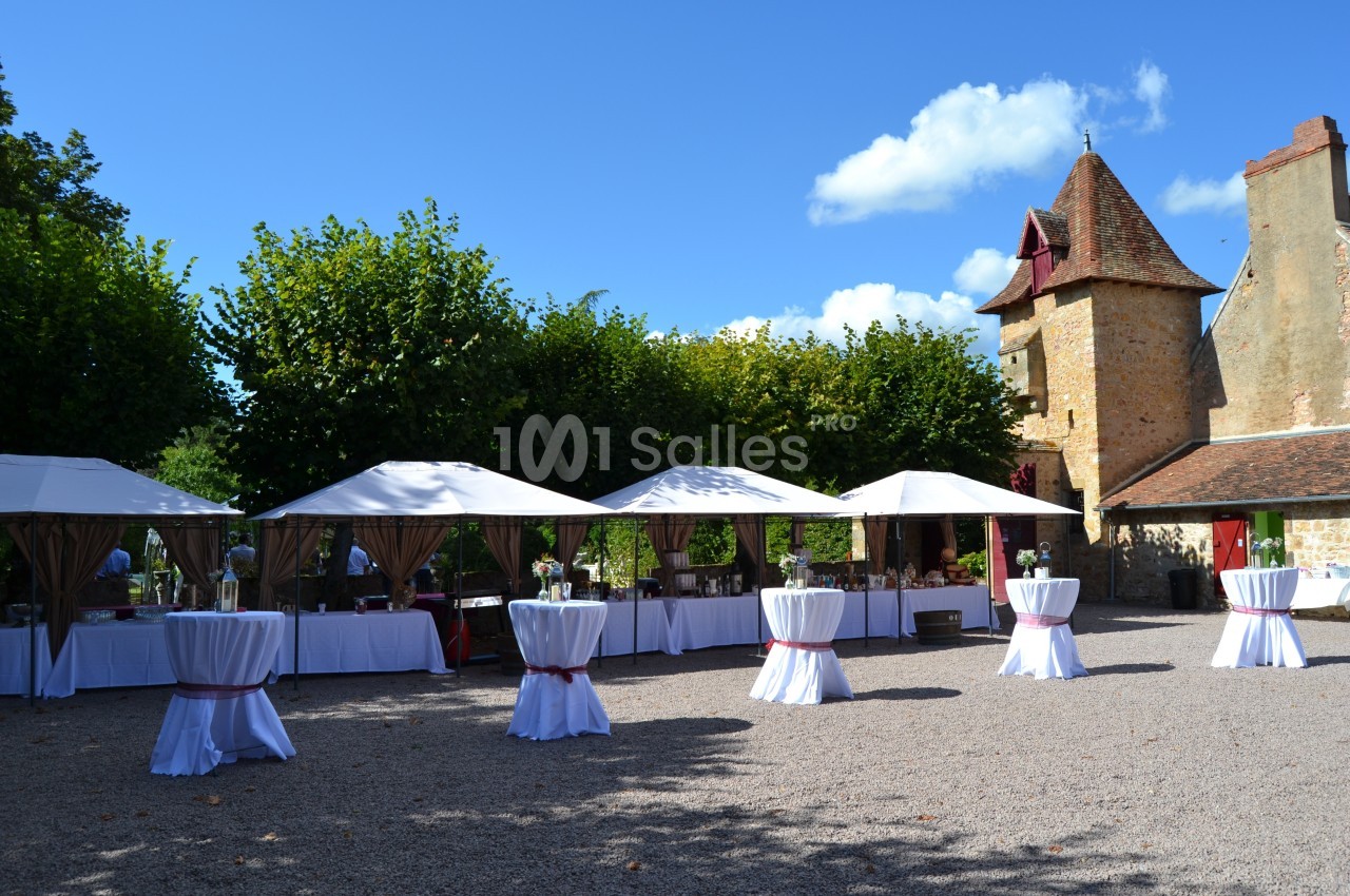 Tentes blanches et tables hautes installées dans une cour pavée devant un bâtiment en pierre sous un ciel dégagé.