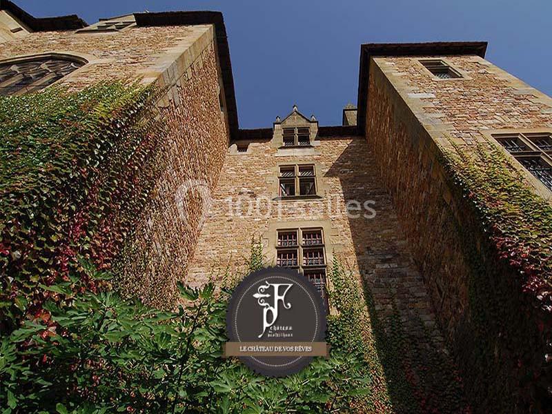 Façade en pierre d'un château entourée de végétation grimpante sous un ciel bleu.