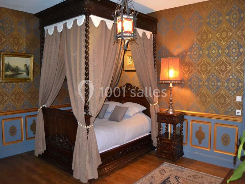 Lit à baldaquin en bois sculpté avec rideaux, dans une chambre au décor classique avec papier peint à motifs et mobilier…