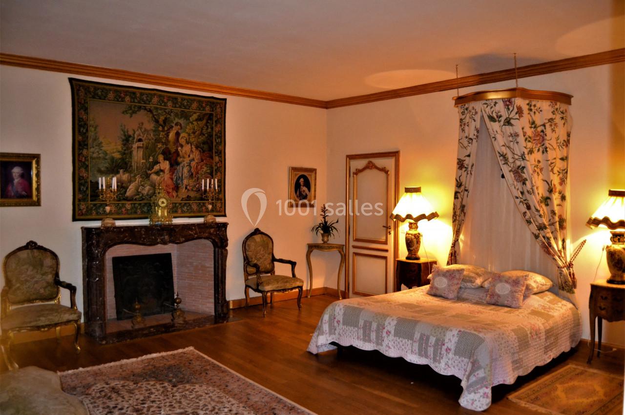 Chambre élégante avec lit à baldaquin, cheminée ornée, tapis et mobilier ancien dans un décor chaleureux.