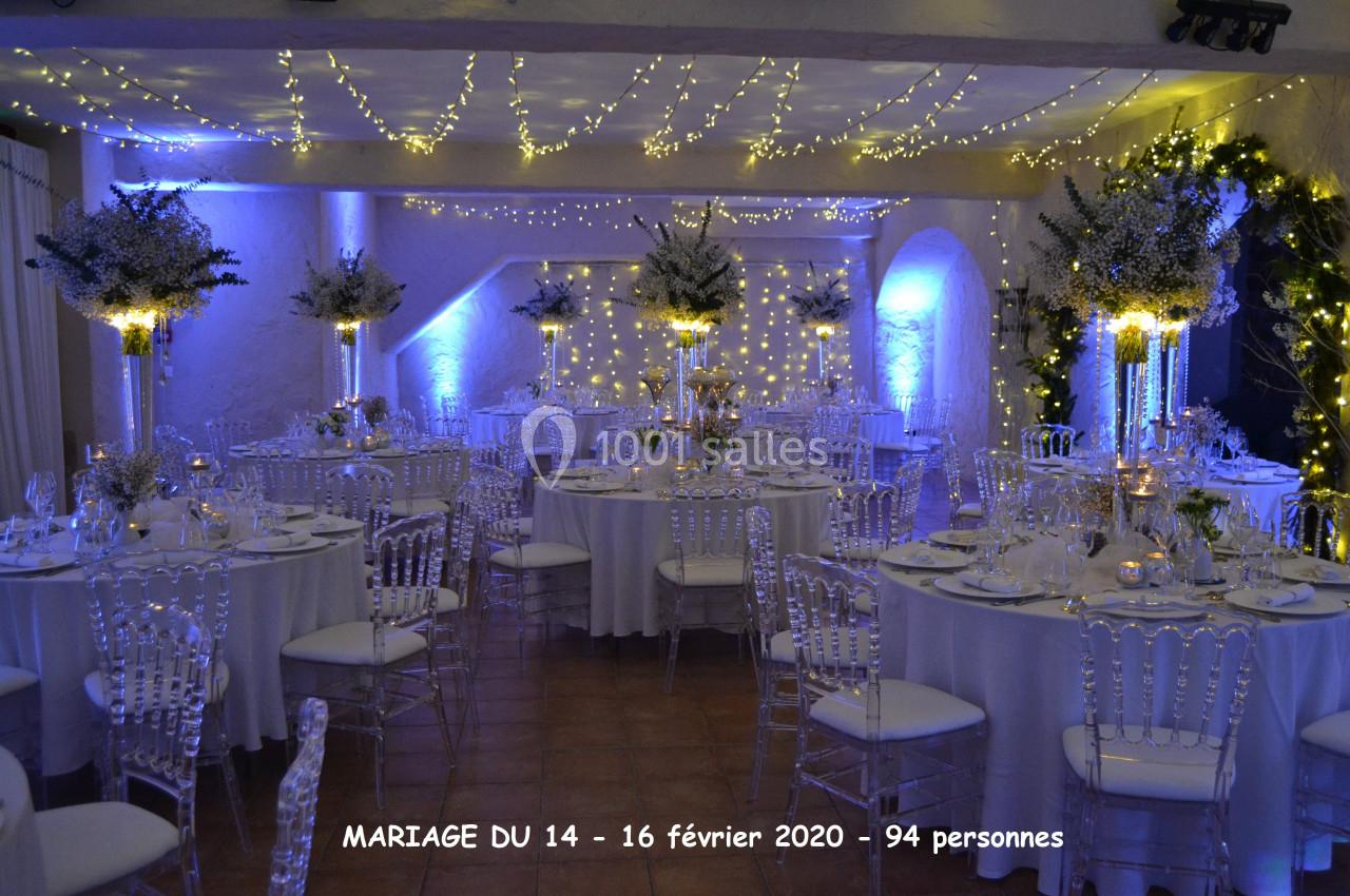 Salle de réception décorée pour un mariage avec tables rondes, chaises transparentes et éclairages féeriques.