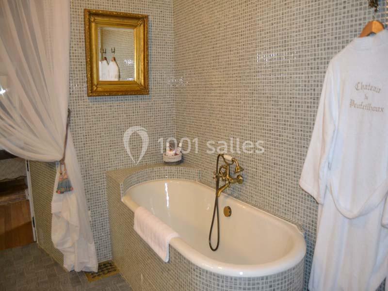 Salle de bain avec baignoire blanche, robinetterie dorée, carrelage mosaïque et miroir encadré au mur.