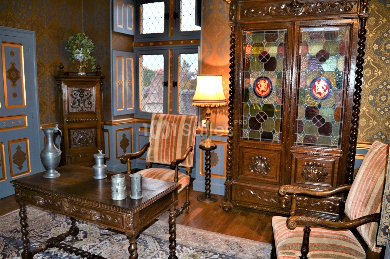 Salle décorée dans un style ancien avec meubles en bois sculpté, vitraux colorés, tapis et lampes d'époque.