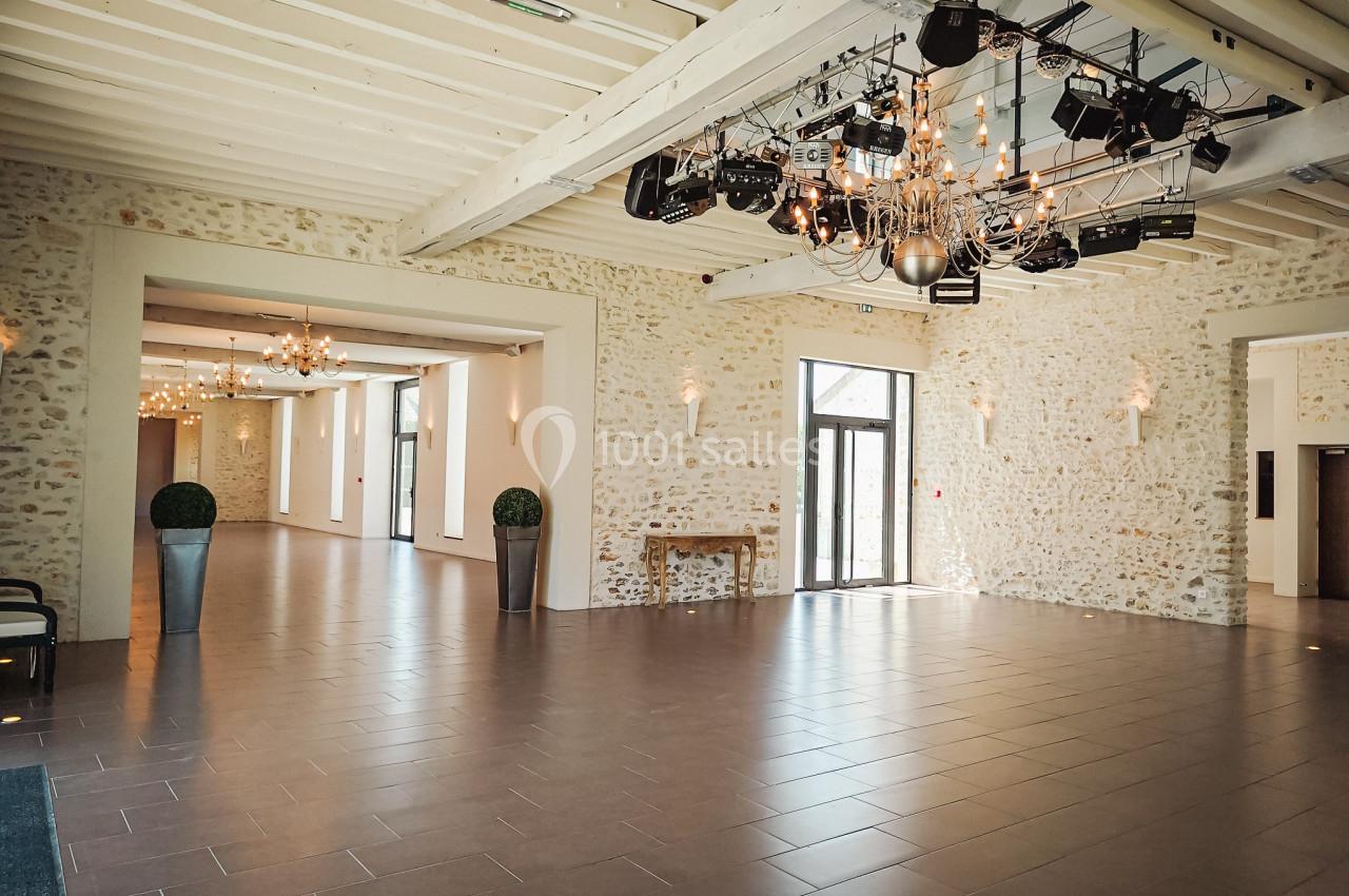 Salle spacieuse avec murs en pierre, grandes baies vitrées, poutres apparentes et éclairage suspendu moderne.