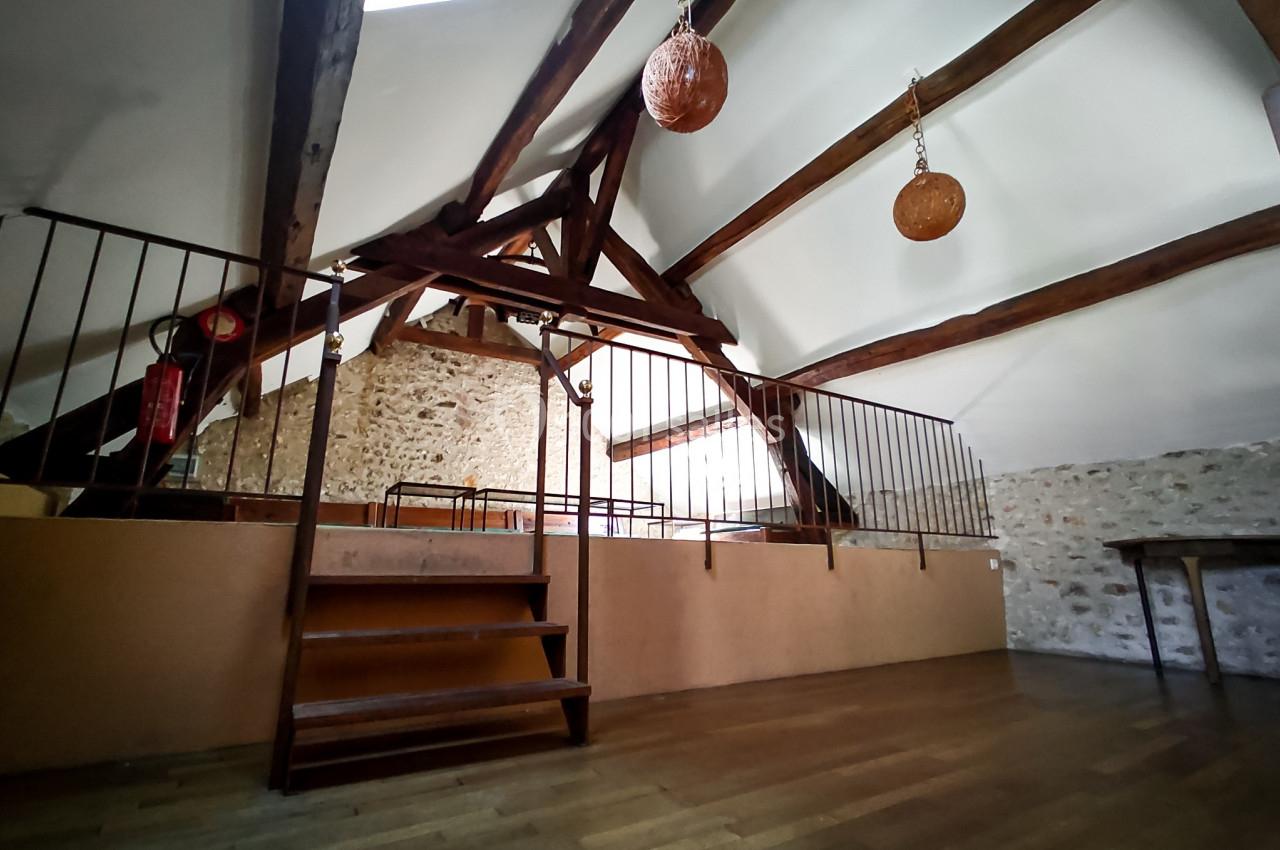 Vue d'une mezzanine avec poutres apparentes, sol en bois, rambarde métallique et murs en pierre.