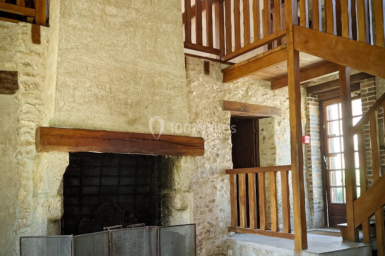Cheminée en pierre dans un intérieur rustique avec mezzanine en bois et poutres apparentes.