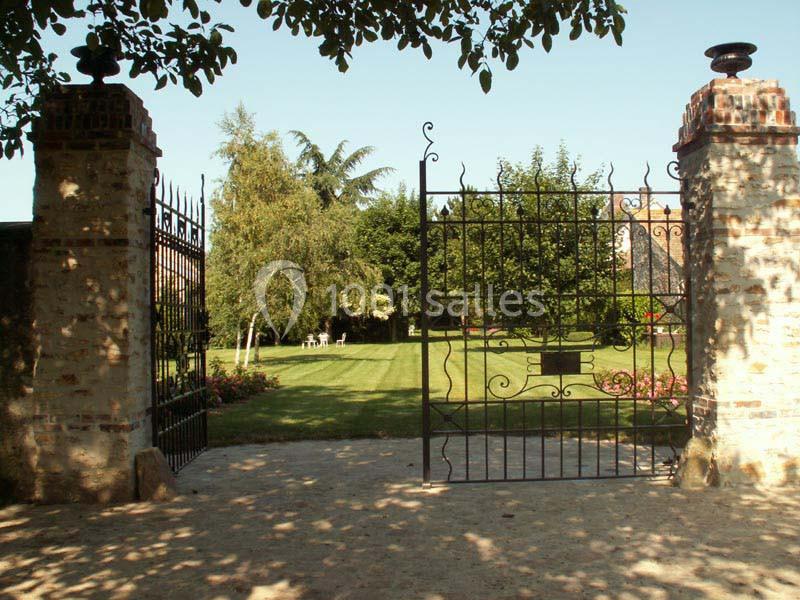 Portail en fer forgé ouvert donnant sur un jardin verdoyant avec pelouse, arbres et fleurs.