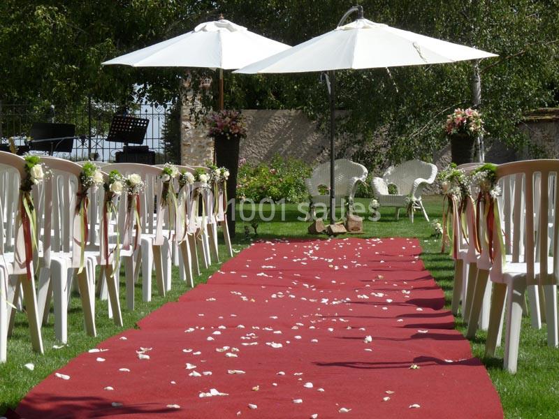 Allée centrale avec tapis rouge, chaises décorées et pétales de fleurs, menant à un espace de cérémonie en plein air.