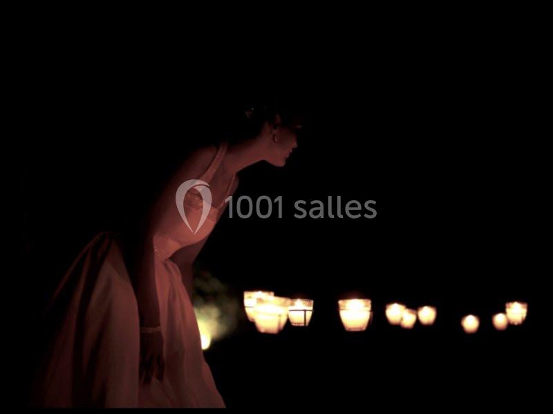 Une femme en robe claire se penche dans l'obscurité, éclairée par une rangée de lanternes lumineuses.