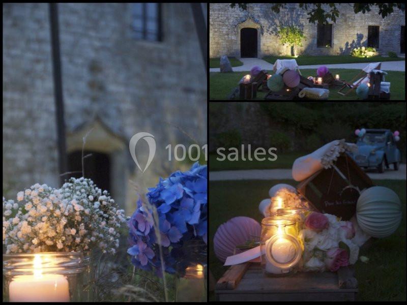 Décorations de mariage en soirée avec bougies, fleurs et lanternes devant un bâtiment en pierre et une voiture ancienne.