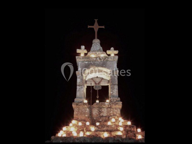 Monument en pierre éclairé par des bougies, avec une croix au sommet, dans un environnement nocturne.