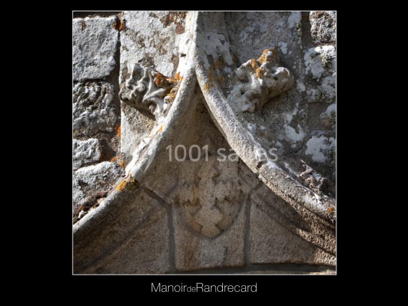 Détail sculpté en pierre d'un blason et de motifs floraux sur une façade ancienne en pierre.