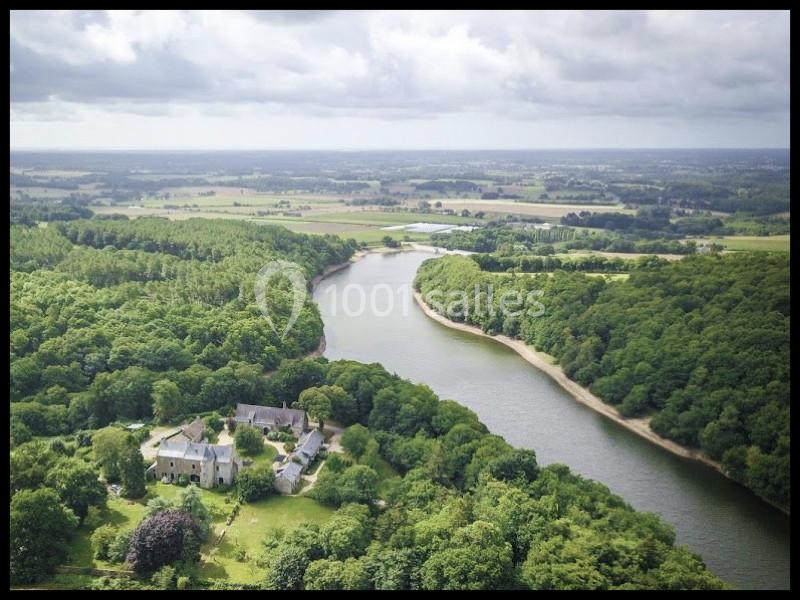 Vue aérienne d'une rivière sinueuse entourée de forêts et de prairies avec un domaine historique au premier plan.