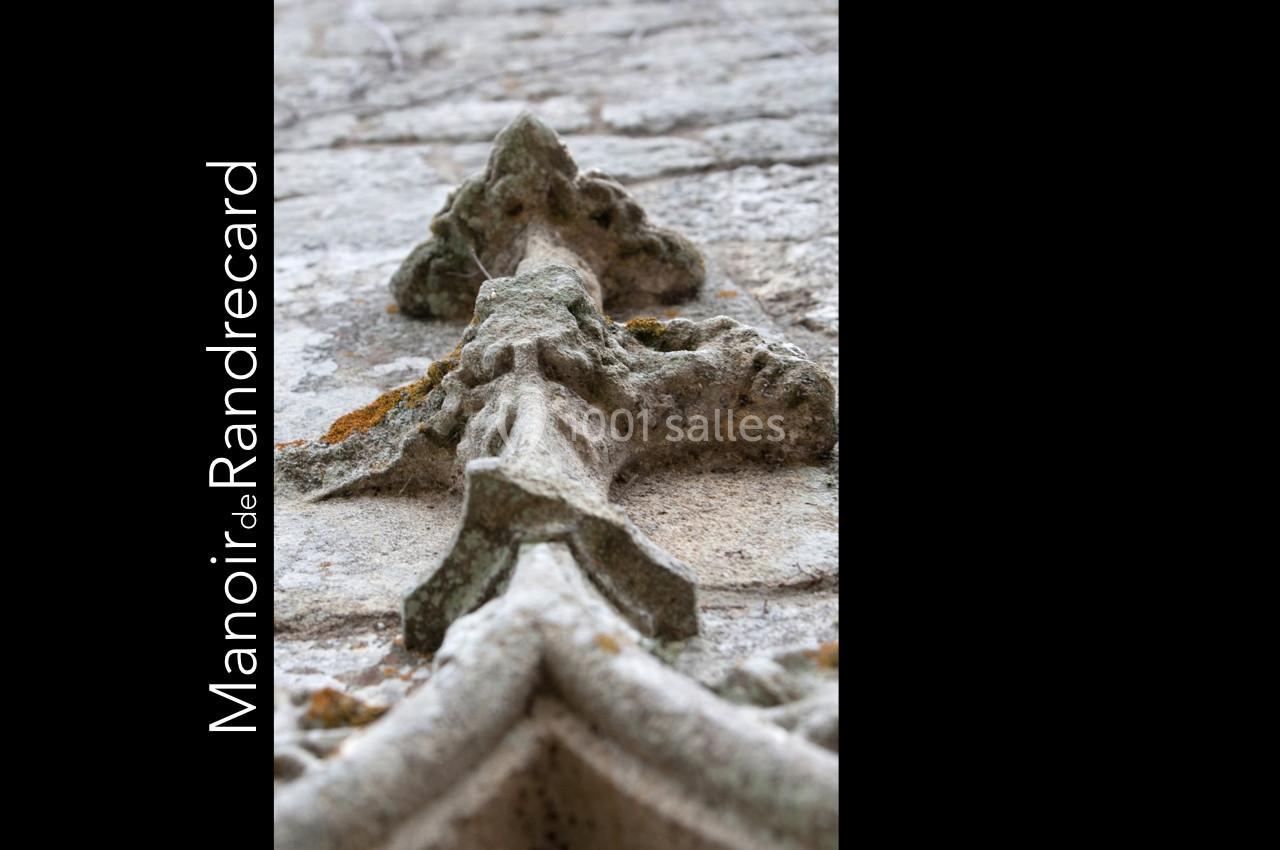 Détail sculpté en pierre d'une façade ancienne, avec une inscription verticale ’Manoir de Randrecard’.