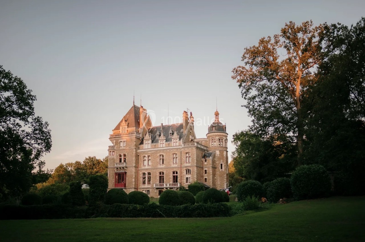 Château ancien entouré de jardins verdoyants et d'arbres, sous un ciel clair en fin de journée.