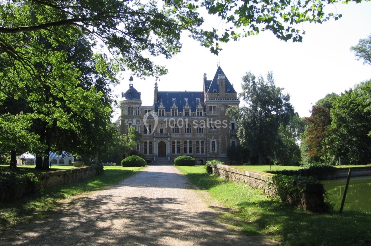 Allée bordée d'arbres menant à un château en pierre entouré de verdure sous un ciel dégagé.