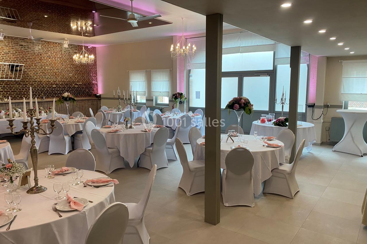 Salle de réception élégamment décorée avec des tables rondes, nappes blanches, chandeliers et éclairage tamisé.