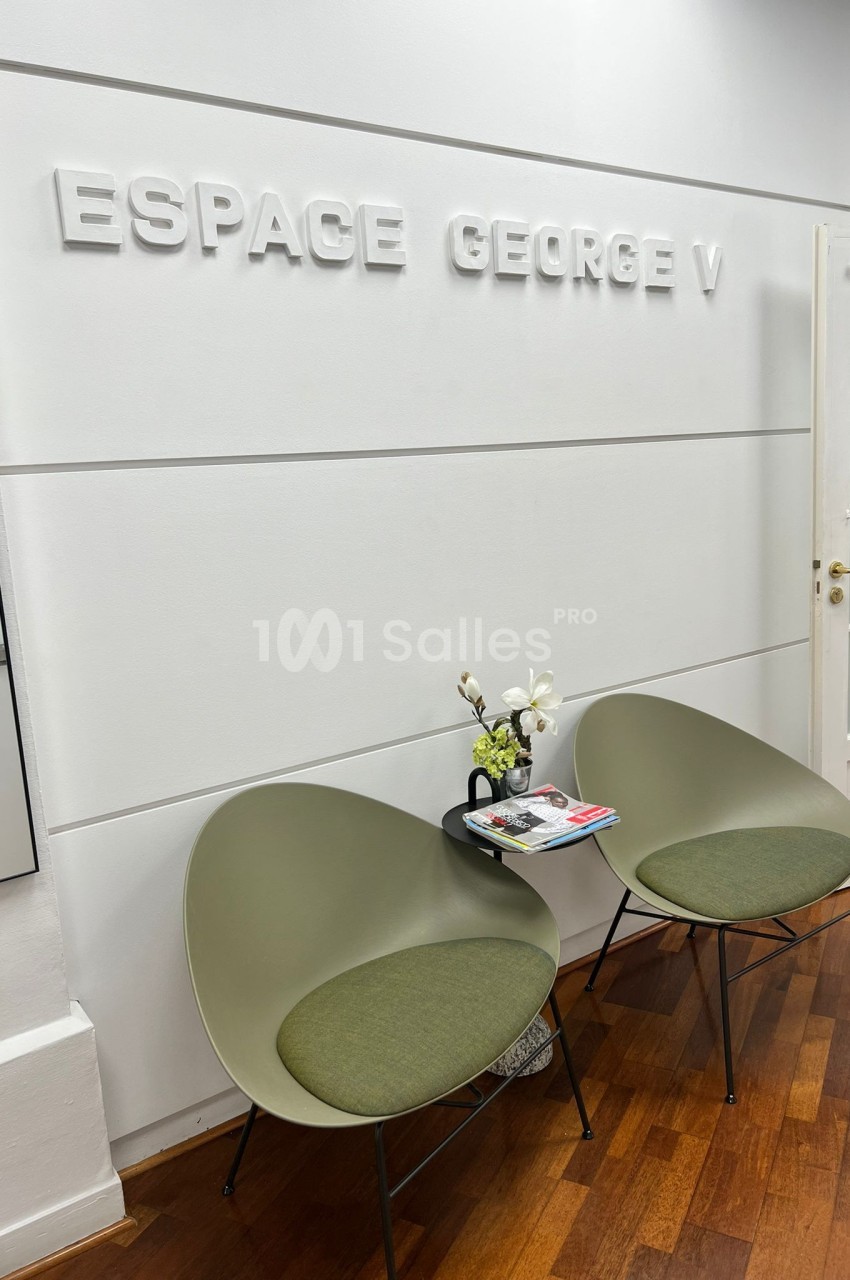 Deux fauteuils verts autour d'une petite table avec des magazines et une fleur, dans un espace lumineux marqué ’Espace…